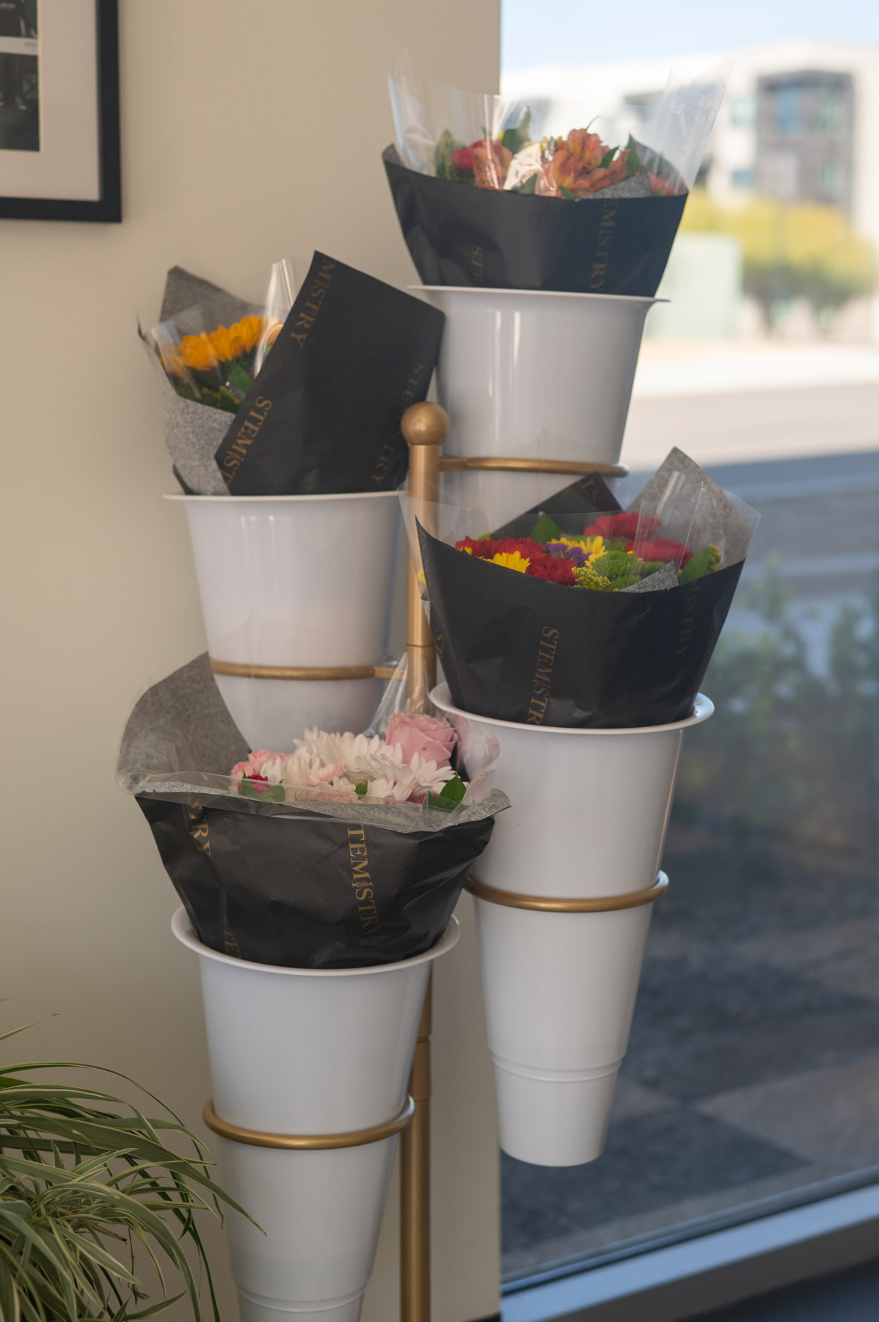 Grab-and-go bouquets in black Stemistry wrap displayed in gold-banded cone vases