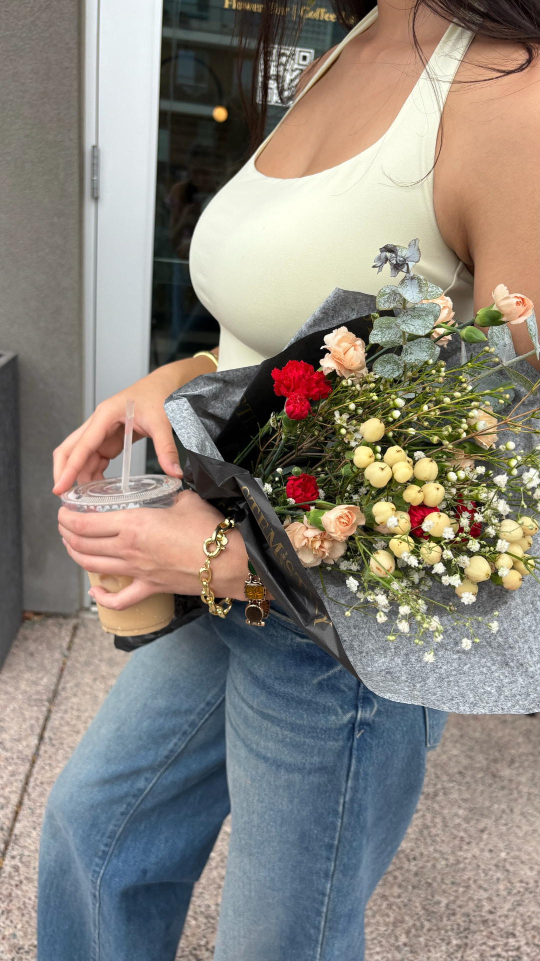 A guest leaving Stemistry with an iced latte in one hand and a black-wrapped bouquet of carnations, hypericum berries, and baby's breath in the other